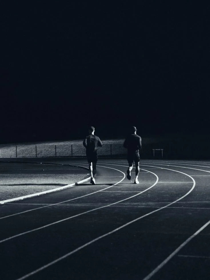 Two runners training on a track after dark